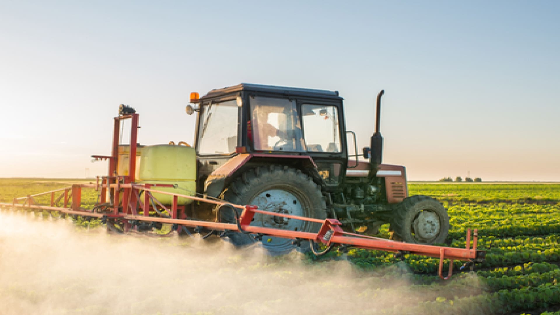 Tractor spraying pesticides on vegetable field with sprayer at spring
